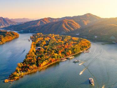 Nami Island near Seoul is lit up by warm sunset colours, with boats navigating the waters around the island