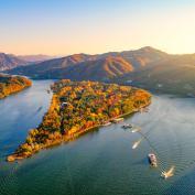 Nami Island near Seoul is lit up by warm sunset colours, with boats navigating the waters around the island