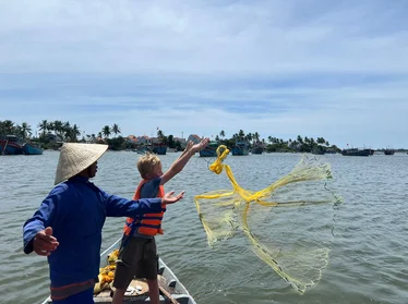 A child throwing a fishing net into the sea during an experience with a local on a family holiday adventure in Southeast Asia