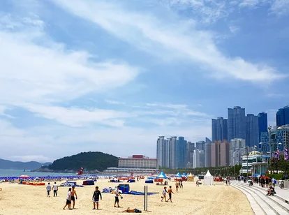 People walking along sandy beach with skyscrapers of Busan in background 