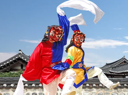 Two traditional folk dancers wearing masks dance in front of hanok houses in South Korea