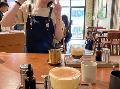 Close-up of Vietnamese egg coffee on a wooden table in a rustic café, with a cheerful barista posing in the background.