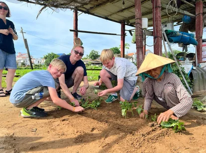 A father and his two children planting crops at a farm-stay on a family trip to Southeast Asia