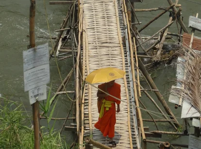 Laos Luang Prabang monk with an umbrella crossing bamboo bridge across the Nam Khan River