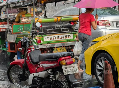 A tuk tuk and woman with an umbrella in Bangkok Thailand during rainy season