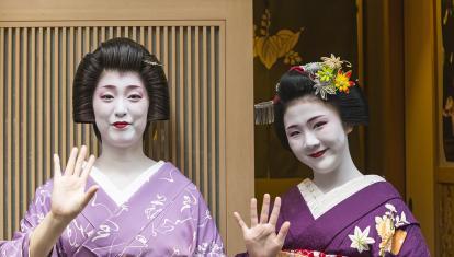 Two geisha girls smiling and waving at the camera in Kyoto