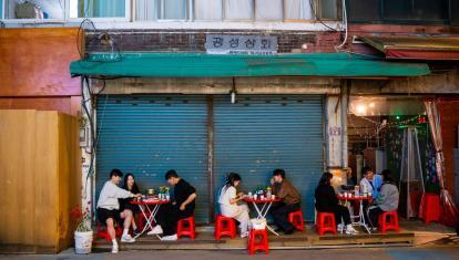 Local South Koreans enjoying food whilst sitting outside on red stools in a street restaurant