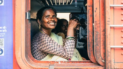 Woman smiling from a train window, the train is red and she's accompanied by fellow passengers inside