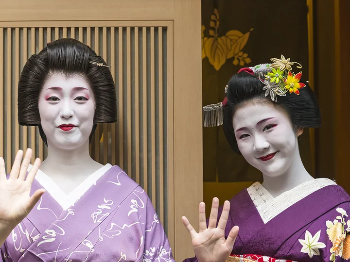 Two geisha girls smiling and waving at the camera in Kyoto 