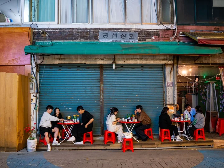 Local South Koreans enjoying food whilst sitting outside on red stools in a street restaurant