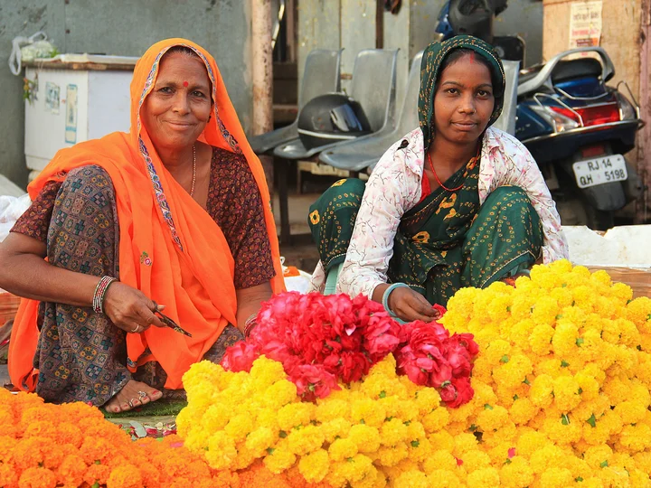 two women selling orange, red and yellow flowers
