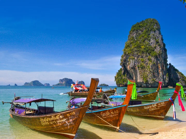Boats parked in an azure beach surrounded by karst rock formations in Krabi, Thailand
