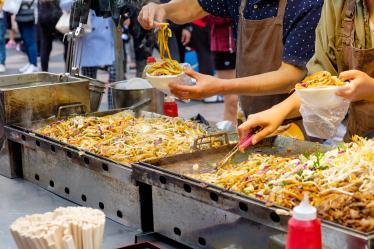 Street food vendor spooning vegetable noodles into takeaway bowl 