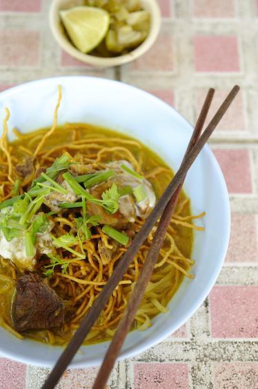 Bowl of curry noodles with chopsticks and lime to garnish 
